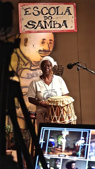 Mestra tocando tambor na gravação da websérie "Escola do Samba".