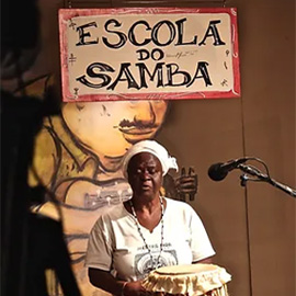 Mestra tocando tambor na gravação da websérie "Escola do Samba".